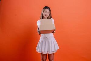 young asian female model in white top smiling to camera both hands holding and giving 2 plain cardboard boxes, standing on orange background. for delivery, gift, expedition, service, package concept photo