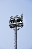 Tall floodlight stadium lamp post tall metal structure from behind view isolated on vertical blue sky background. photo