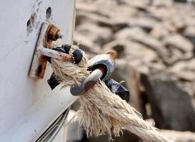 Worn out white rope and metal hinge holder object isolated on horizontal ratio outdoor rocks environment background. photo