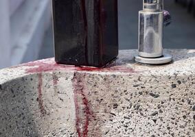 Overflowing red purple colored liquid soap from plastic bottle dispenser isolated on horizontal ratio stone sink and metal water faucet background. photo