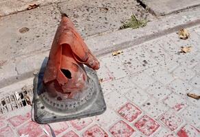 One old and broken orange plastic traffic cone object isolated on horizontal ratio brick stone flooring background. photo
