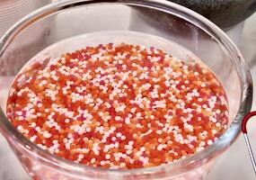 Sweet and delicious small round white, orange, and red jelly dessert toppings in glass bowl isolated on horizontal ratio white table background. photo