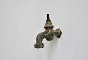 Old and aged rusty iron water faucet with missing valve handle part isolated on horizontal ratio white wall background. photo
