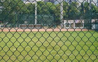 Green metal net chain link baseball field fence barrier isolated on horizontal green grass environment background. photo