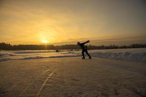A man skates on a frozen lake, golden light of the setting sun in the background photo