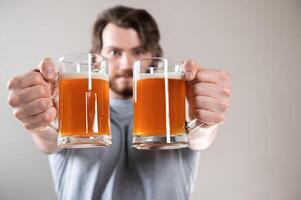 Close-up of man's hands with two beer mugs, face blurred in background photo
