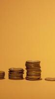 Several stacks of coins are neatly organized in ascending order on a vibrant yellow background, symbolizing financial growth and investment. The arrangement highlights different levels of wealth. video