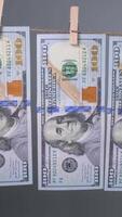 1 cem dólar contas estão pendurado com prendedores de roupa contra uma cinzento pano de fundo, exibindo seus Projeto e detalhes proeminentemente para inspeção ou mostrar. video