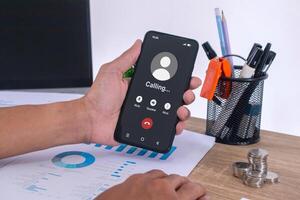 Hand holding a mobile phone with outgoing call screen. Call someone with a voice call at workplace. photo