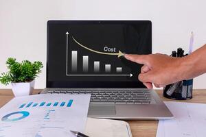 Hand pointing to laptop screen to show graph of cost reduction. Cost reduction analysis in the workplace. photo