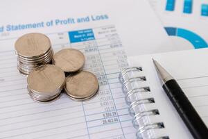 Close up view of stack of coins, notebook, and pen on top of financial data paperwork photo