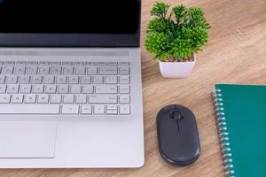 Close up view of work desk with laptop computer, notebook, mouse, and plants in pot. photo