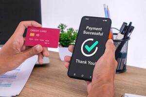 Hand holding credit card and using smartphone to make online payment. Successful payment message on smartphone screen. photo