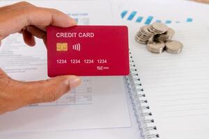 Hand holding a credit card on his desk with paperwork, blank notebook, and coins photo