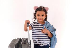 A little Asian girl smiling while holding a jacket on her shoulders and her suitcase photo