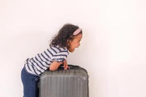 Attractive little Asian girl in striped shirt and wearing headband posing with a suitcase photo