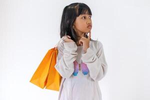 A little Asian girl posing with one hand pointing to her chin while holding paper shopping bags. Thinking about something to buy. photo