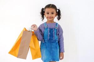 A cheerful little Asian girl posing while holding paper shopping bags in her right hand on a white background photo