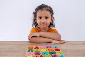 Asian little girl crossing her arms on the table with wooden alphabet letters for playing and learning photo