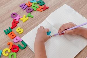 A little girl learning to write letters in a notebook with wooden alphabet letters on the table photo