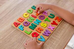 Hands of little girl assembles wooden alphabet letters puzzle on a table photo