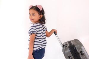 A cute little Asian girl wearing a headband and posing while pulling a suitcase photo