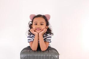 A little Asian girl posing with a suitcase on a white background, both hands on chin photo