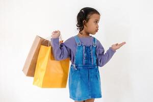 Excited little Asian girl looking and pointing at something to the side while holding a paper shopping bag photo