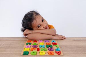 A little Asian girl sitting at a table with wooden alphabet letters while resting her head on her arms photo