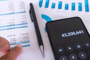 Close up view of financial data report on work paper with pen and calculator app on mobile phone. An auditor analyzes financial report data. photo