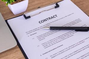 Contract documents on the wooden table with pen and laptop photo
