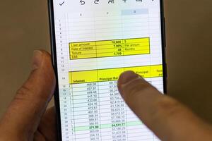 Man scrolling an excel sheet on the phone screen showing bank loan amortization table. Banking photo