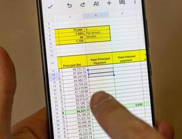 Man scrolling an excel sheet on the phone screen showing bank loan amortization table. Banking photo
