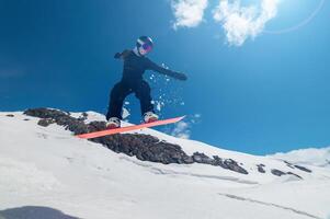 Female snowboarder jumping off a ski jump and doing a trick. Amazing shot of a snowboarder flying in the air and grabbing a trick against the backdrop of snowy mountains photo