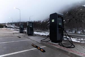 Electric car charging station, row of gas stations stands against the backdrop of mountains in fog in winter, cloudy weather photo