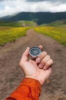 Compass in hand against the background of a mountain road, vertical photo. Choosing a path in travel and hiking photo
