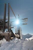 An unfinished metal structure of a cable car station high in the mountains. The structure is covered in snow and the sun shines through its ceilings photo