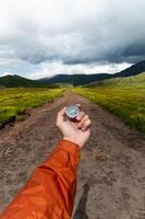 Compass in hand against the background of a mountain road, vertical photo. Choosing a path in travel and hiking photo