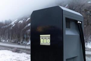 Close-up Electric car charging station, row of gas stations stands against the backdrop of mountains in fog in winter, cloudy weather photo