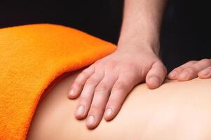 Hands of a masseur apply oil to the back of a young woman and massage her back with gentle movements, close-up. The client is covered with a towel in intimate areas photo
