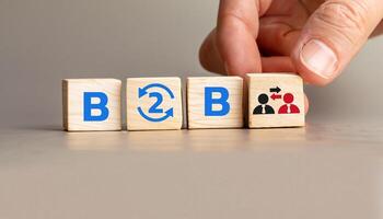 B2B Concept with Wooden Cubes Displaying Business to Business Collaboration, Hand Arranging Cubes with Arrows and People Icons, Symbolizing Partnerships and Exchanges. photo