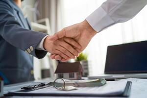 Two men shake hands in front of a desk with a contract on it photo