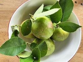 Close up of green ripe lemon fruit and green leaves in bowl on the wooden table background, Meyer lemon, Citrus Lemon photo