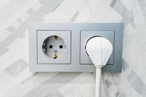A white plug is inserted into a wall socket for electrical supply photo