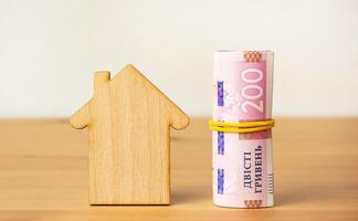 The concept of paying utility bills. Ukrainian bills of 200 hryvnias and a wooden house. Side view. photo