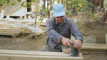 A skilled worker carefully operates a sander, shaping wooden planks for an outdoor project surrounded by greenery and natural light. The atmosphere is tranquil and focused. video