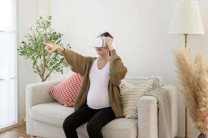 Pregnant woman wearing vr box using future technology for entertainment in living room photo