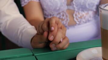 The bride and groom tenderly hold hands at a table in a cafe video