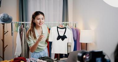 Portrait of Cheerful woman influencer is live streaming sell clothes on social media or blogging in home studio. Remote buying, Online shopping. photo