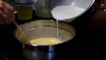 Female hands add milk to bowl of beaten eggs with mixer. Waffle cookie recipe step by step. Hand mixer beats eggs, milk. Beating dough with mixer. Whipping dough for pancakes video